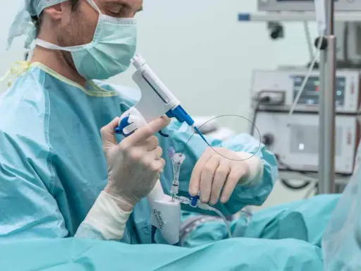 Chirurg w masce i rękawiczkach trzyma przyrząd medyczny do biopsji.