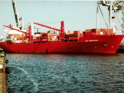 Rotes Containerschiff "Cap Finisterre" im Hafen, beladen mit vielen Containern, Kräne im Hintergrund.
