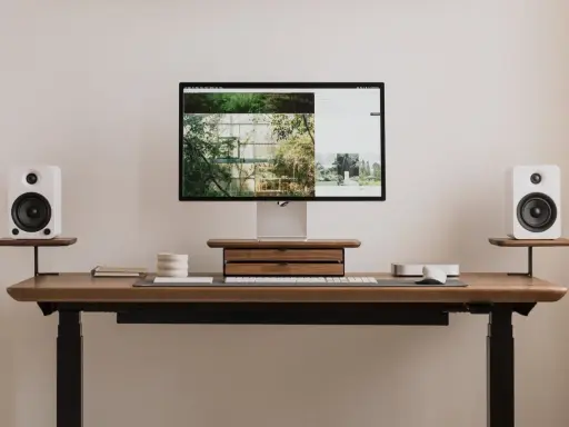 Minimalistyczny blat zamiast biurka inspiracje: monitor, białe głośniki, drewniana szuflada, klawiatura i myszka.