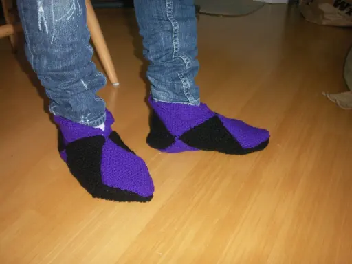 Ett par stickade innetofflor i lila och svart, med jeans till. Perfekta för mysiga hemmakvällar.