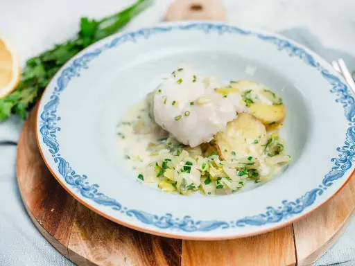 En vacker tallrik med pocherad fisk, potatis och vitkål i en krämig sås, garnerad med gräslök.