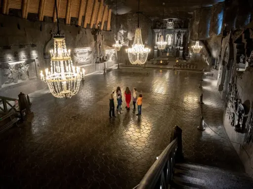 Grupa turystów w podziemnej kaplicy Kopalni Soli w Wieliczce, oświetlonej kryształowymi żyrandolami.
