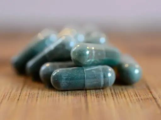 Pile di capsule verdi su un tavolo di legno. Si possono prendere due antibiotici insieme, ma sempre sotto controllo medico.