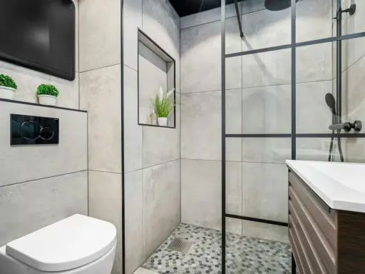 Mampara de ducha con diseño de ventana, separando el espacio de la ducha. Baño moderno con inodoro y lavabo.