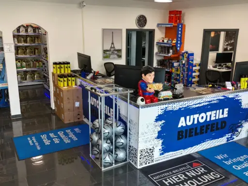 Autoteile-Shop mit Theke, Regalen voller Autoteile, einem Superman-Aufsteller und Fußmatten.