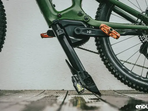 Zielony rower elektryczny z pomarańczowymi pedałami. Widoczny mechanizm, który ułatwia zrozumienie, jak wyjąć baterię z roweru elektrycznego.