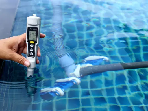 Mano mide salinidad de piscina con cloración salina. El medidor muestra 3160 ppm, indicando posibles problemas.