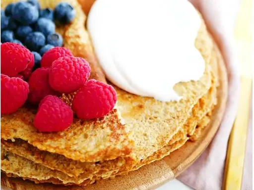 En hög med nyttiga pannkakor toppas med grädde, hallon och blåbär. En perfekt frukost eller mellanmål.