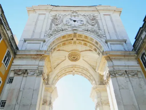 Der Arco da Rua Augusta in Lissabon, ein imposanter Triumphbogen mit einer Uhr und kunstvollen Verzierungen, ragt majestätisch in den blauen Himmel.