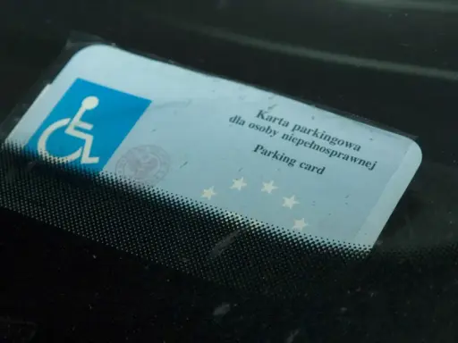 Niebieska karta parkingowa dla osoby niepełnosprawnej z symbolem wózka inwalidzkiego, umieszczona za przednią szybą samochodu.