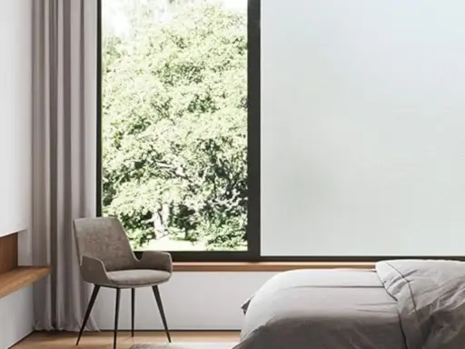 Habitación con cama, sillón y ventana con vidrio mate que filtra la luz del sol y la vegetación exterior.