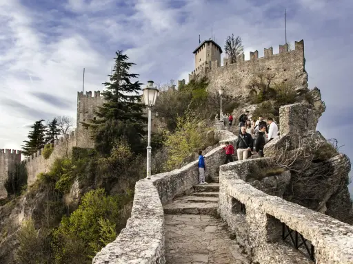 Sentiero roccioso verso le torri di San Marino, un viaggio nella storia. Turisti salgono la scalinata che porta alle antiche fortificazioni.