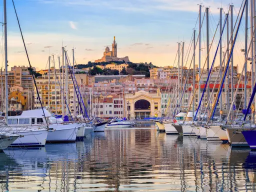 Barche a vela ormeggiate nel porto di Marsiglia, con la Basilica di Notre-Dame de la Garde sullo sfondo. Un'ottima vista per chi cerca cosa vedere a Marsiglia vicino al porto.