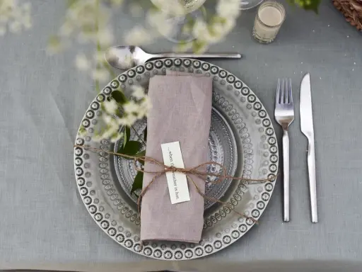 Vacker dukning med linneservetter, blommor och en korg med bröd. Perfekt för en sommarfest.