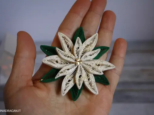 Un fiore di carta in quilling, perfetto per un tutorial di quilling natale. Dettagli dorati e petali bianchi e verdi.