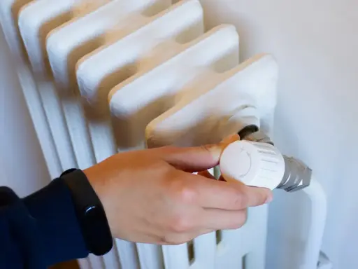 Mano ajustando el termostato de un radiador blanco. Controlar la temperatura ayuda a saber cuanto cuesta la calefaccion al mes.