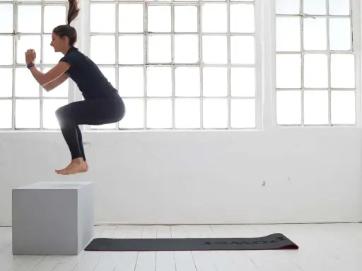 Frau macht **box jumps** in einem hellen Raum mit großen Fenstern.