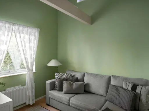 Sofá gris con cojines, lámpara y cortinas blancas junto a pared verde. ¡Excelentes ideas pintar casa con este tono fresco!