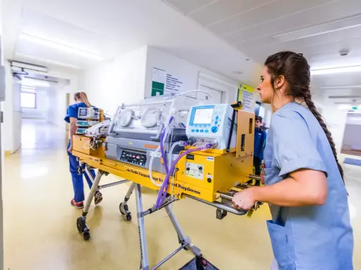 Infermiera spinge un'incubatrice mobile in un corridoio ospedaliero. Quanto tempo in terapia intensiva neonatale è cruciale per questi piccoli pazienti.