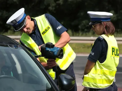 Policjanci w kamizelkach odblaskowych mierzą prędkość samochodu radarem.