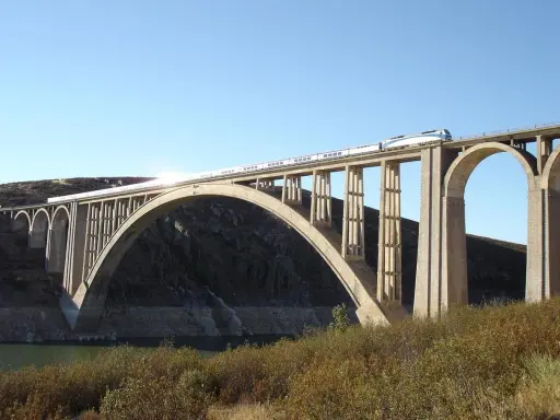 Un tren de alta velocidad cruza un imponente puente arco de hormigón sobre un embalse.