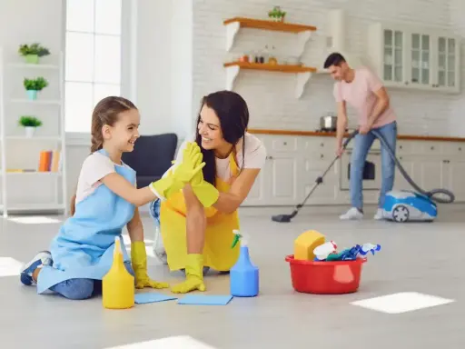 Mama i córka świętują udane porządki. W tle tata odkurza. To świetny przykład, jak obowiązki 9 latka w domu mogą być wspólną zabawą.