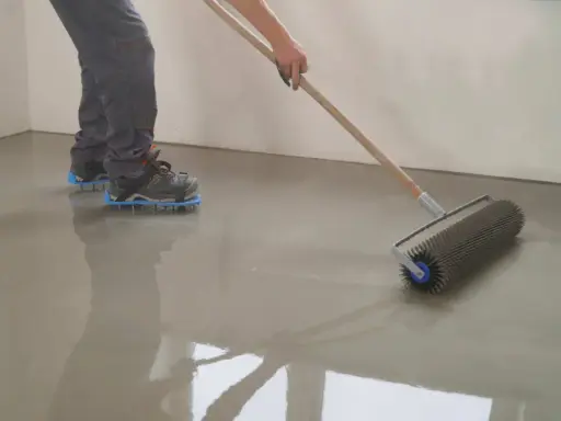 Persona con calzado de púas usando un rodillo para nivelar un suelo recién vertido.
