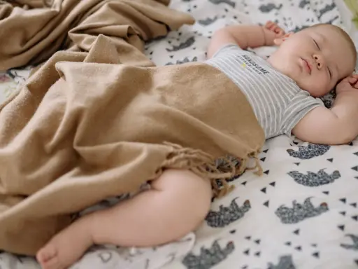 Bebé durmiendo plácidamente, envuelto en una manta de tonos tierra. Las medidas del arrullo bebé son ideales para su comodidad.