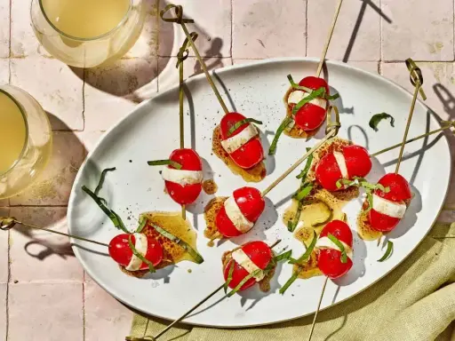 Szybkie przekąski na ognisko: pomidorki koktajlowe z mozzarellą i bazylią na patyczkach, polane sosem.