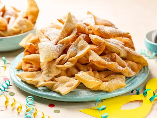 Un piatto colmo di chiacchiere, dolci tipici di Carnevale, cosparse di zucchero a velo. Festa e gusto, ecco cosa si mangia a Carnevale!