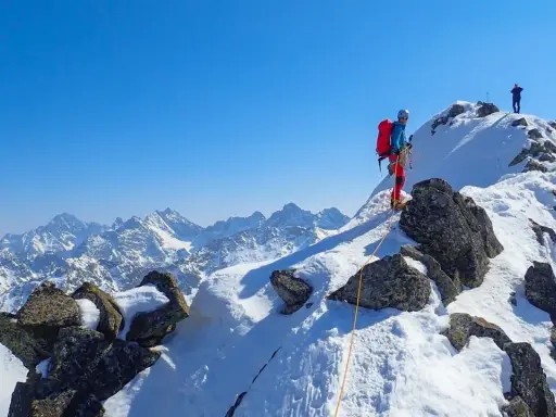 Wspinaczka zimą na Orlą Perć. Dwóch alpinistów na ośnieżonym szczycie, jeden z nich asekurowany liną.
