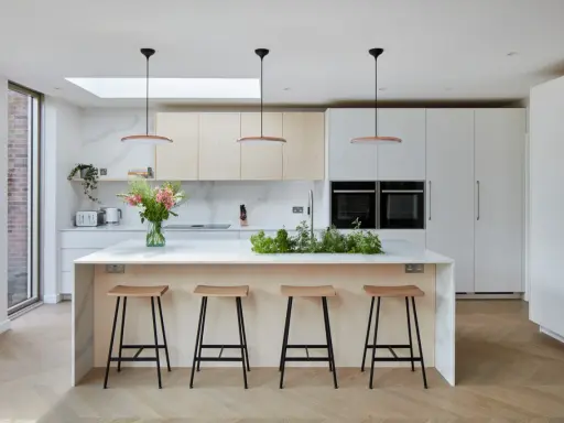 Cuisine moderne avec îlot central, tabourets en bois et une niche ouverte intégrée dans les placards.