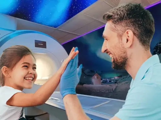 Uśmiechnięta dziewczynka daje "piątkę" lekarzowi w niebieskiej rękawiczce. W tle aparat do rezonansu magnetycznego dla dzieci i bajkowy krajobraz.