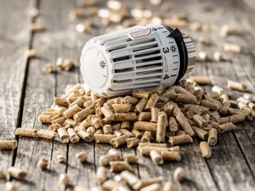 Ein Thermostat auf einem Haufen Holzpellets. Die Frage "wie lange heizt man mit 1 tonne pellets" wird hier visuell thematisiert.