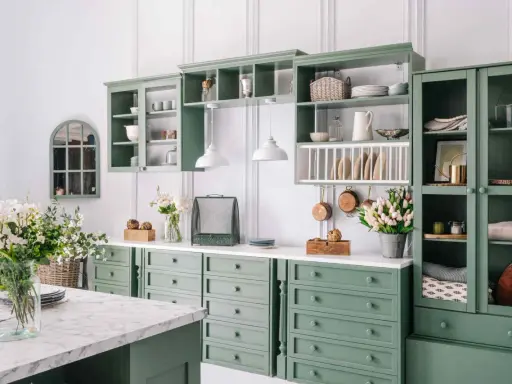 Cucina in stile provenzale casa con mobili verdi, pentole in rame appese e fiori freschi.