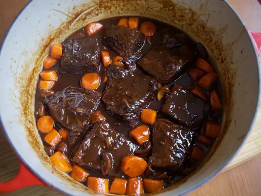Boeuf bourguignon casero en olla roja, con trozos de carne tierna, zanahorias y champiñones en una rica salsa.