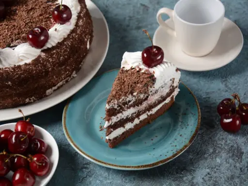 Una porción de tarta Selva Negra, con capas de bizcocho de chocolate, nata y cerezas, decorada con virutas de chocolate y una cereza encima.