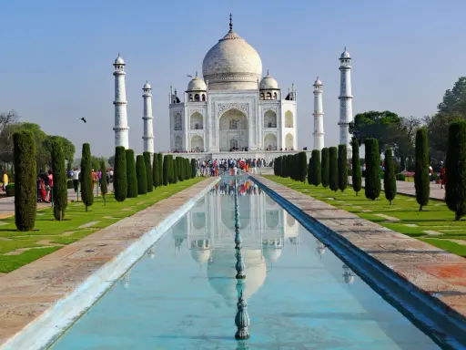 Majestatyczny Taj Mahal w Indiach odbija się w spokojnej wodzie, otoczony zielonymi ogrodami i strzelistymi cyprysami.