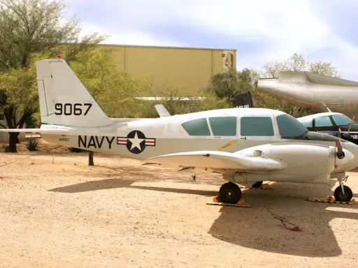 Ein zweimotoriges Piper-Flugzeug der US Navy mit der Kennung 9067 steht auf einem staubigen Flugplatz.