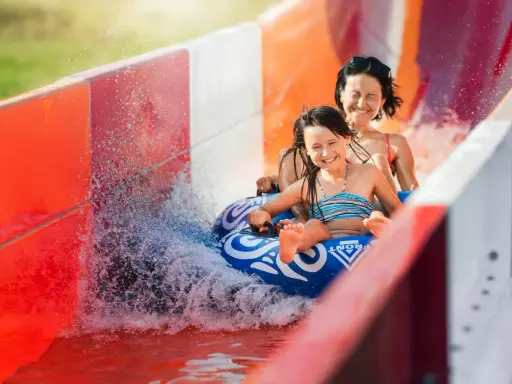 Mama i córka z uśmiechem zjeżdżają na pontonie po zjeżdżalni wodnej. Włochy ciekawostki dla dzieci: zabawa w aquaparku to świetny pomysł na wakacje!