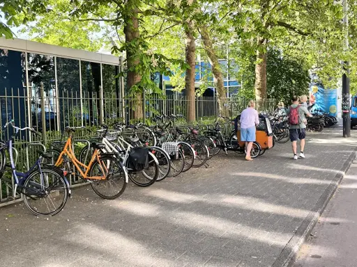 Viele Fahrräder stehen am Straßenrand, ein Mann mit Kind auf dem Arm und eine Frau mit Lastenrad gehen vorbei. Eine echte Stadt der kurzen Wege.
