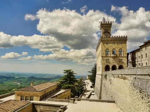 Torre del Campanone e Palazzo Pubblico nel **San Marino centro**, con vista panoramica sulle colline verdi sotto un cielo azzurro e nuvoloso.