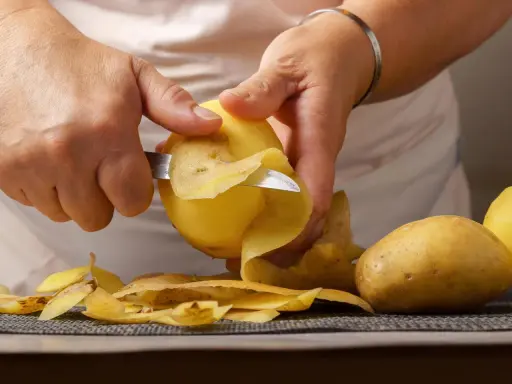 Hände schälen Kartoffeln für die Zubereitung. Bald sind die Kartoffeln gar und bereit zum Genuss.