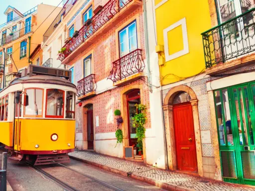 Gelber Straßenbahn fährt durch eine enge Gasse mit bunten Häusern. Ein typisches Bild der Umweltzone Lissabon.
