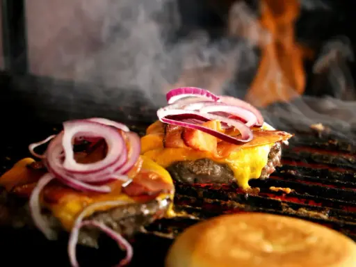 Pyszne burgery z grilla, z rozpływającym się serem i chrupiącym boczkiem, unoszą się w dymie.