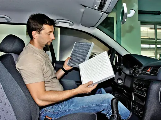 Mężczyzna w kabinie Renault Megane 3 porównuje stary i nowy filtr kabinowy, przygotowując się do jego wymiany.