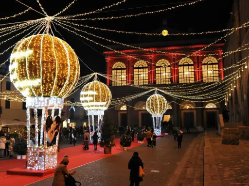 Luci scintillanti e palloni luminosi creano un'atmosfera magica per un week end a Rimini. Persone passeggiano su un tappeto rosso, ammirando le decorazioni natalizie.