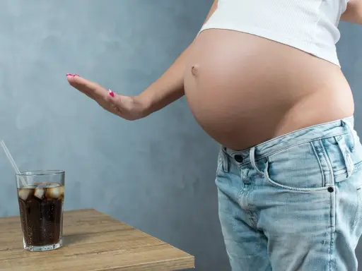 Schwanger und verzichtet auf Cola. Eine Hand weist ein Glas Cola mit Eis und Strohhalm ab.