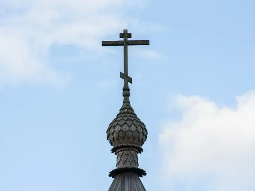 Drewniany krzyż na kopule cerkwi, symbol religii w Gruzji, na tle błękitnego nieba z chmurami.
