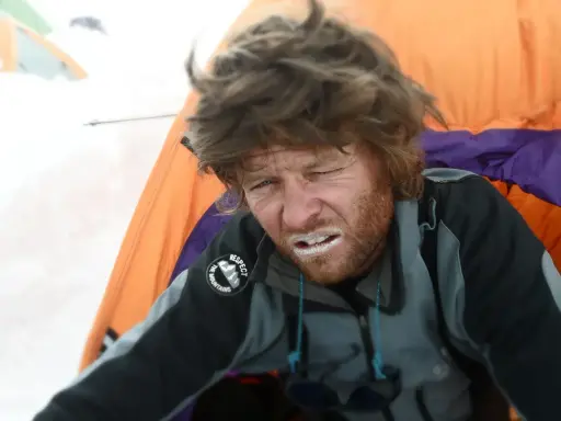 Zmęczony alpinista z białym proszkiem na ustach, być może lek na chorobę wysokościową, w namiocie na śniegu.
